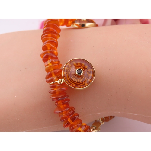 183 - 9ct Gold Amber Bracelet. Composed of graduated amber beads with applied 9ct gold mounts charms and c... 