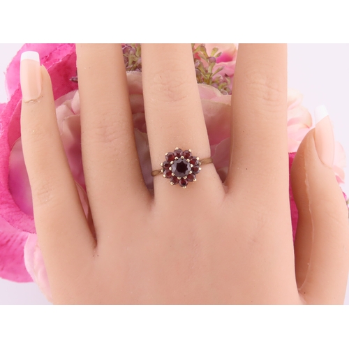 191 - A 9 carat gold garnet cluster ring, the central garnet surrounded by a halo of matching garnets in a... 