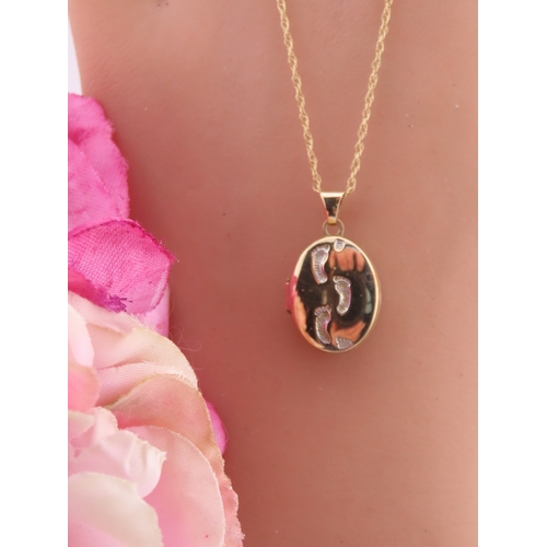192 - A 9 carat gold oval locket, the front decorated with a raised footsteps motif, opening to reveal a g... 