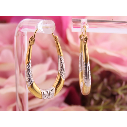 200 - A pair of 9 carat yellow and white gold hoop earrings, of oval form with engraved white gold detaili... 
