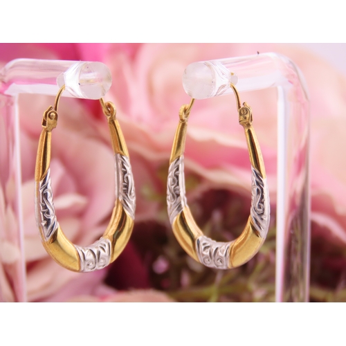 200 - A pair of 9 carat yellow and white gold hoop earrings, of oval form with engraved white gold detaili... 