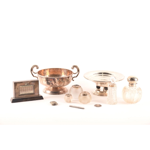 164 - A collection of silver comprising an art deco perpetual calendar, two crystal scent bottles, a trio ... 