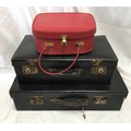Two black compressed cardboard suitcases 60 x 35cms and 50 x 29cms together with a red vanity case.