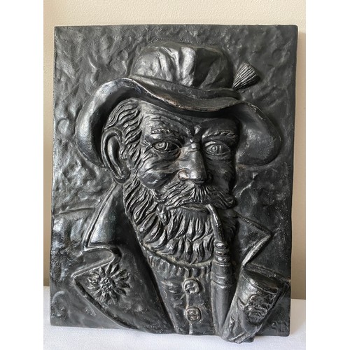 962A - A black cast iron plaque of the Old Man smoking a pipe.