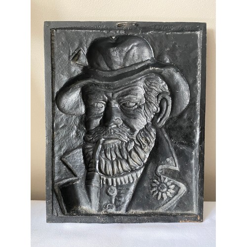 962A - A black cast iron plaque of the Old Man smoking a pipe.