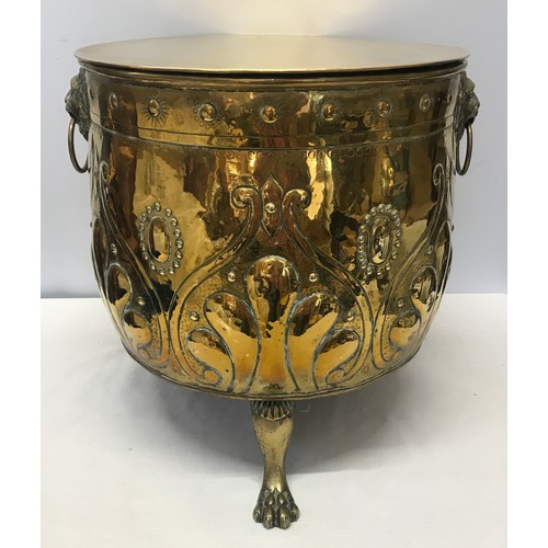 922 - A large brass circular log bucket with embossed decoration, lion head handles, tripod claw feet and ... 