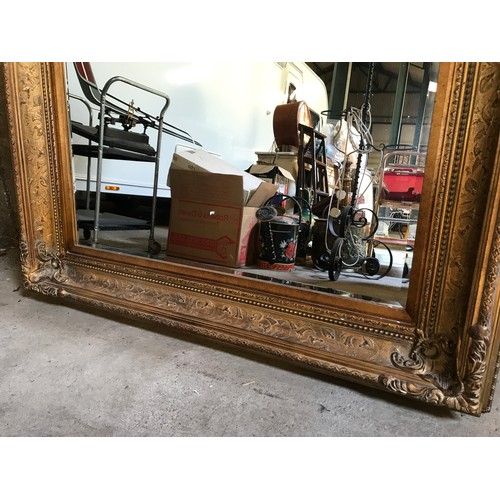 927 - A large gilt framed over mantle mirror with bevel edging. Frame size 122cms x 152cms.