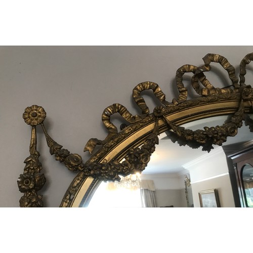 928 - A decorative gilt and gesso framed 19thC oval bevel edged wall mirror. Frame surmounted with bow and... 