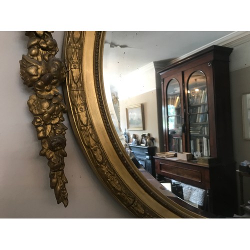 928 - A decorative gilt and gesso framed 19thC oval bevel edged wall mirror. Frame surmounted with bow and... 