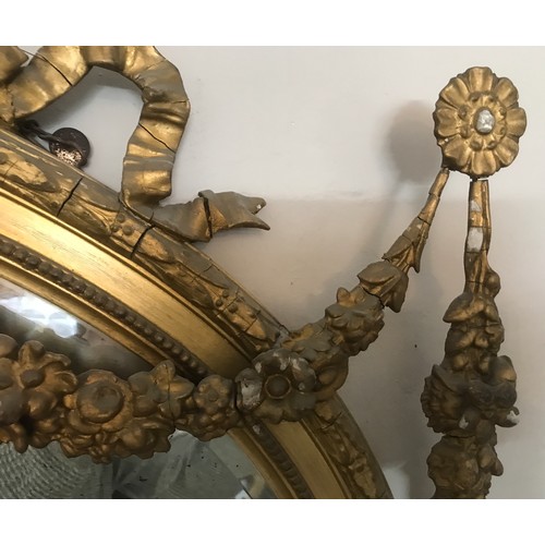 928 - A decorative gilt and gesso framed 19thC oval bevel edged wall mirror. Frame surmounted with bow and... 