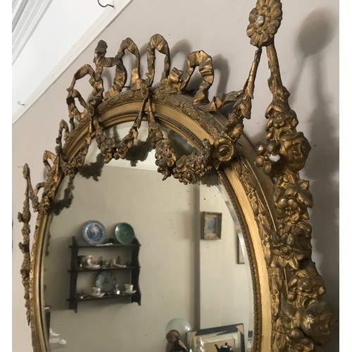 928 - A decorative gilt and gesso framed 19thC oval bevel edged wall mirror. Frame surmounted with bow and... 