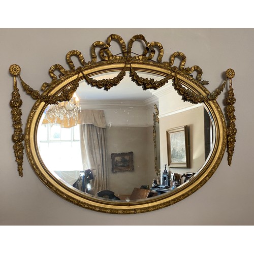 928 - A decorative gilt and gesso framed 19thC oval bevel edged wall mirror. Frame surmounted with bow and... 