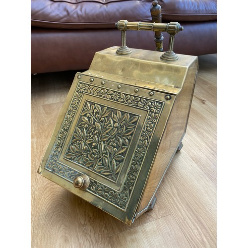 568A - A Victorian brass coal scuttle with floral design cover, raised on panelled feet with liner and shov... 