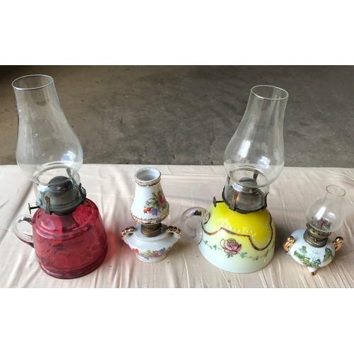 556 - Four oil lamps, one ruby glass, 29cms h including chimney, one yellow white glass floral pattern, an... 