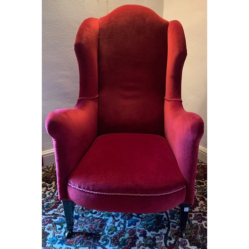 1242 - A winged armchair with square tapered legs to front and upholstered in red velvet and brass castors.