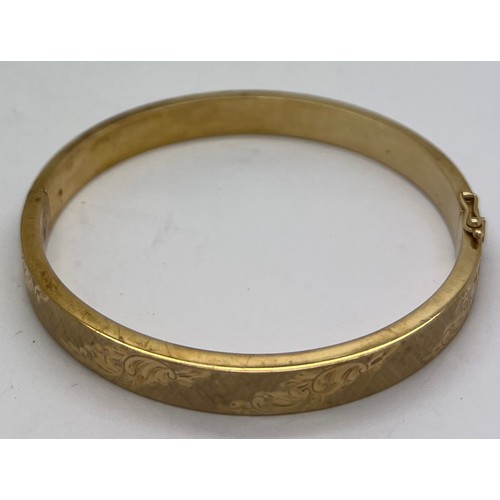 390 - A 9ct gold hinged bangle with engraved decoration. 18gm.