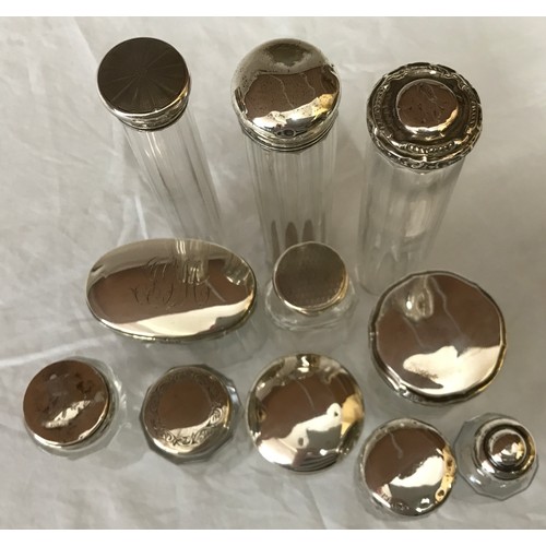 864 - Selection of silver topped glass containers some bearing a cartouche/pattern. Tallest 18cm (7).