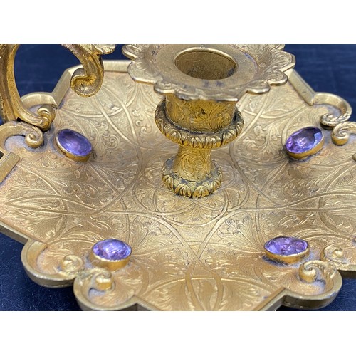 769 - A candlestick holder set with 5 purple coloured stones, centurion head decoration to handle. 11cm w ... 