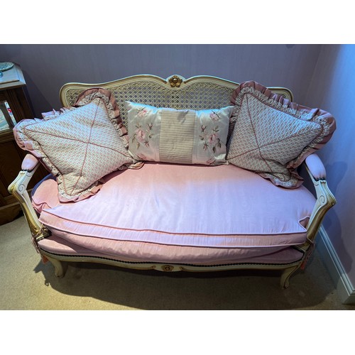 131 - A two seater cream and gilt framed sofa with caned back and upholstered pink cushion. 76cm h x 116cm... 