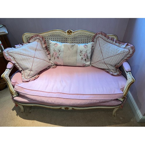 131 - A two seater cream and gilt framed sofa with caned back and upholstered pink cushion. 76cm h x 116cm... 