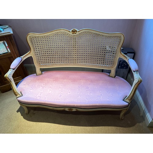 131 - A two seater cream and gilt framed sofa with caned back and upholstered pink cushion. 76cm h x 116cm... 