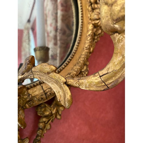 1137 - An ornate gilt plaster wall mirror with bows and floral garlands, 2 candle sconces. 58cm h x 34cm w.