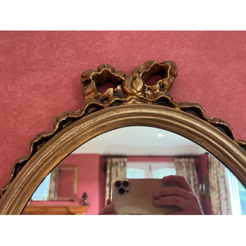 1138 - Two gilt oval wall mirrors, largest with bow 59cm h x 39cm w, smaller bevel edged 33cm h x 24.5cm w.