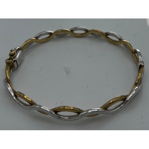 611 - A nine carat yellow and white gold hinged bangle. Weight 10.6gm.