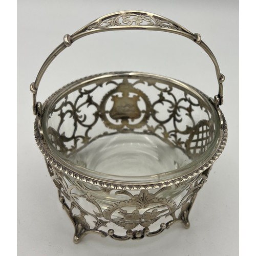 757 - Pierced silver basket with swing handle, vacant cartouche and associated glass liner. Birmingham 190... 