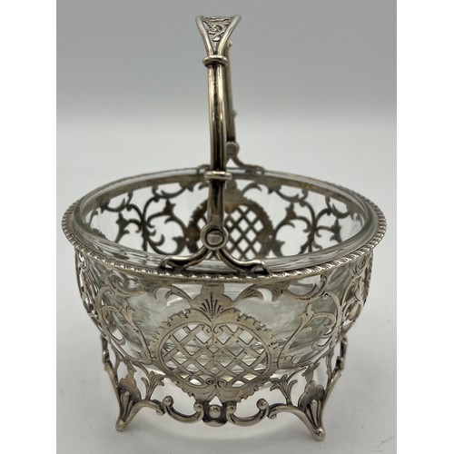 757 - Pierced silver basket with swing handle, vacant cartouche and associated glass liner. Birmingham 190... 