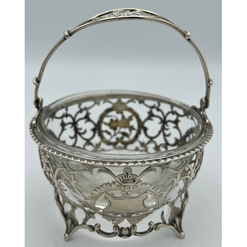 757 - Pierced silver basket with swing handle, vacant cartouche and associated glass liner. Birmingham 190... 