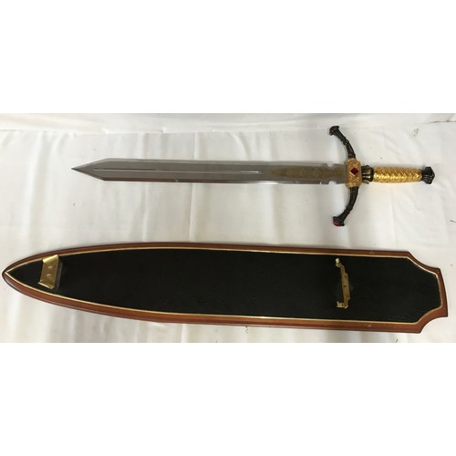 1100 - A large heavy decorative sword on wooden plaque with gold coloured handle and pattern to bottom of b... 