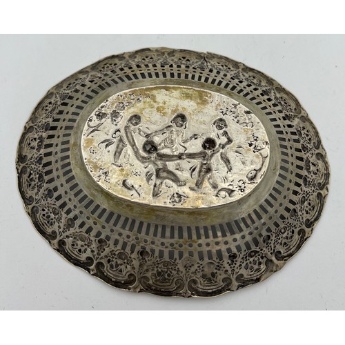 704 - A German silver oval dish depicting dancing cherubs with a pierced border. Size 18 x 14.5cm. Weight ... 