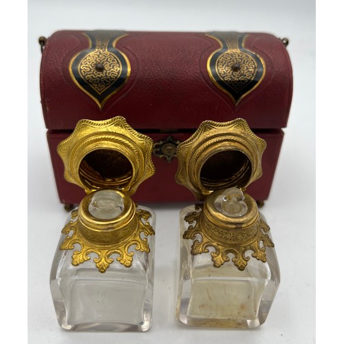 1043 - Red leather covered casket containing two glass and gilt metal scent bottles with painted tops and i... 