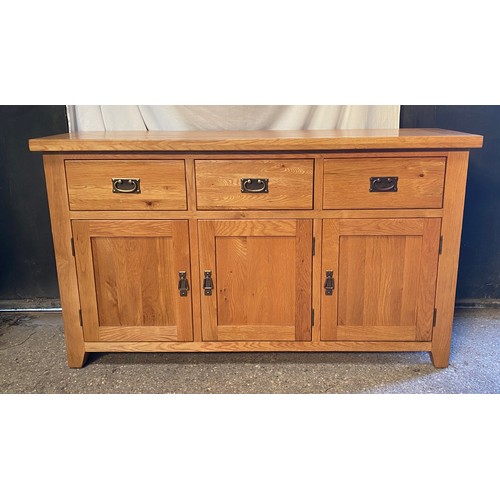 79 - An oak sideboard, three drawers over three doors. 87 h x 149 w x 44cm d.