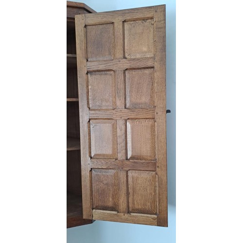 174 - An oak Robert Thompson Mouseman corner cupboard with recessed mouse, panelled door with three shelve... 