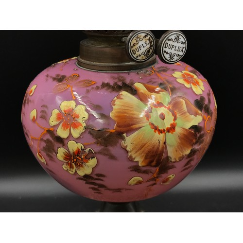 761 - An oil lamp decorated in hand painted yellow flowers on a pink background marked Duplex with clear g... 