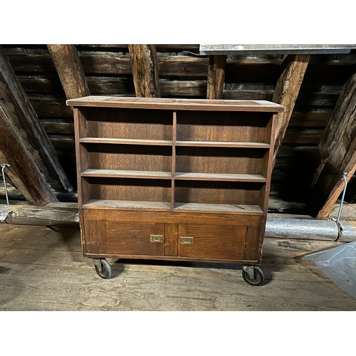 181 - An oak double sided library book case on wheels with cupboards to one side and top storage compartme... 