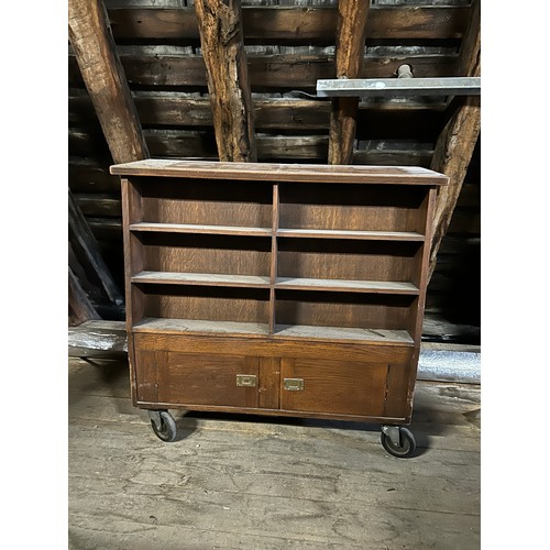 181 - An oak double sided library book case on wheels with cupboards to one side and top storage compartme... 