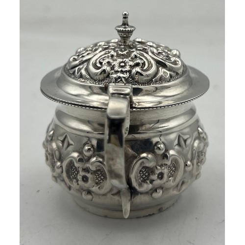 63 - A small bellied silver mustard pot with a repeating pattern of rococo Cs reversed and containing flo... 