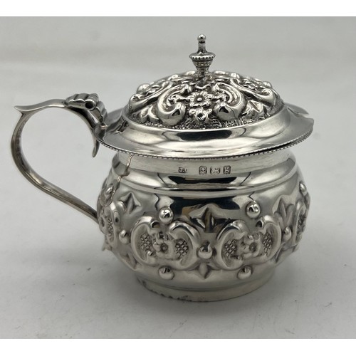 63 - A small bellied silver mustard pot with a repeating pattern of rococo Cs reversed and containing flo... 