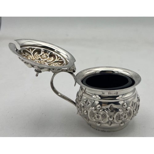 63 - A small bellied silver mustard pot with a repeating pattern of rococo Cs reversed and containing flo... 