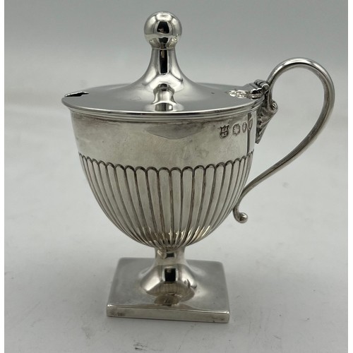 66 - An urn shaped silver mustard pot on a square base, the lower half of the body fluted, the lid rising... 