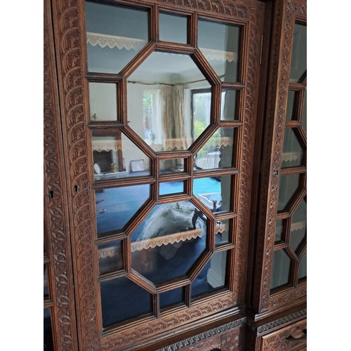 53 - A very highly carved hardwood display cabinet/ bookcase, three glazed doors over a base of drawers a... 