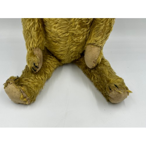 1077 - An early 20thC straw filled Teddy with glass amber eyes black stitched nose, mouth and claws, swivel... 