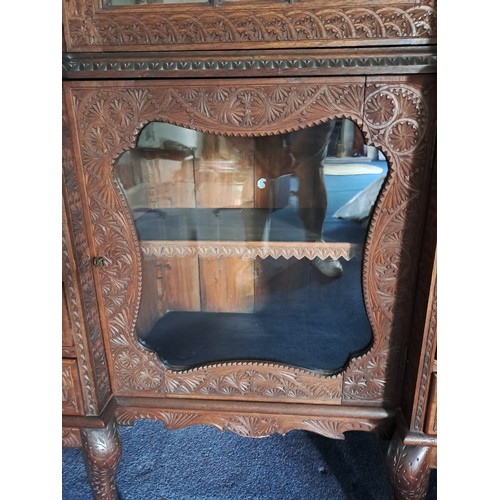 69 - A very highly carved hardwood display cabinet/ bookcase, three glazed doors over a base of drawers a... 