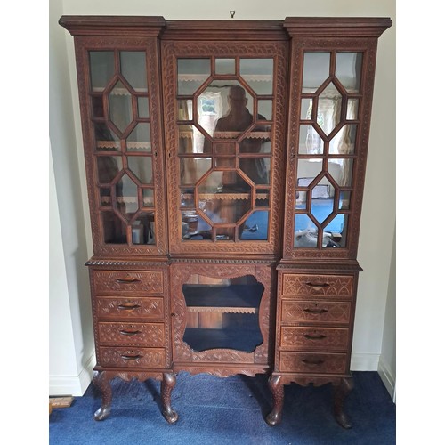 69 - A very highly carved hardwood display cabinet/ bookcase, three glazed doors over a base of drawers a... 