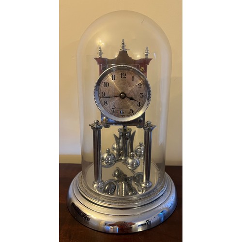 1007 - A chrome anniversary clock under a glass dome, complete with key. 30cm h.