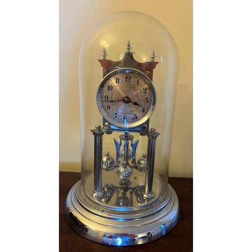 1007 - A chrome anniversary clock under a glass dome, complete with key. 30cm h.