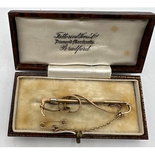 475 - A nine carat gold bar brooch in the form of a riding crop with safety chain, in fitted presentation ... 